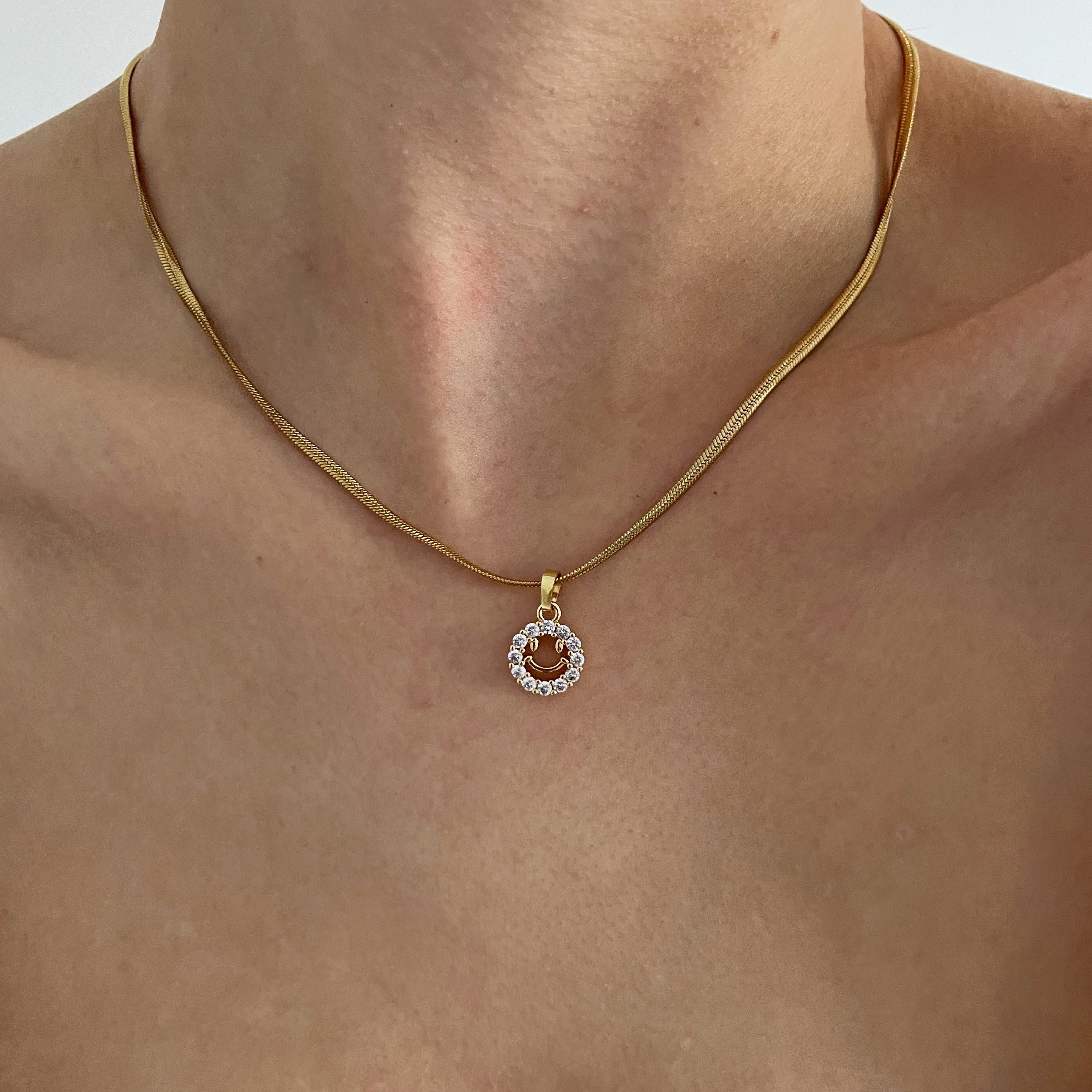 Trendy gold necklace with a cute smiley face pendant.